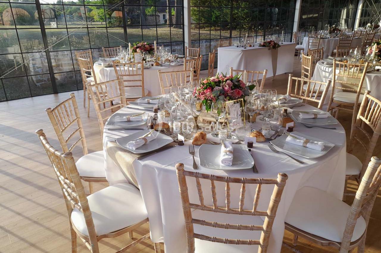 Table ronde décorée pour un événement, avec nappes blanches, vaisselle élégante et centre de table floral.