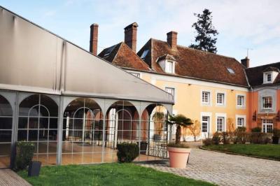 Chambre lumineuse avec lit double, fauteuil gris, bureau en bois, fenêtre à carreaux et poutres apparentes.