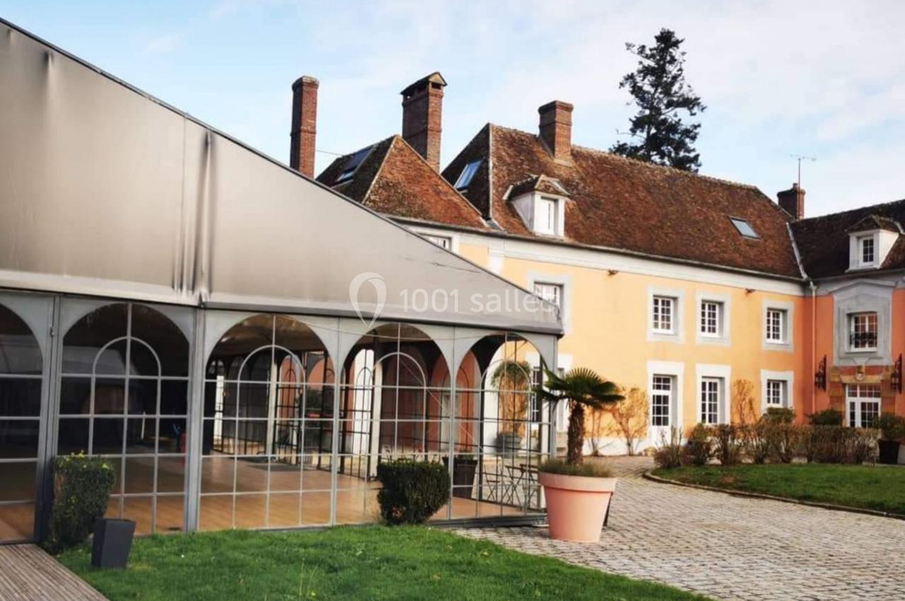 Bâtiment ancien avec toit en tuiles, véranda moderne attenante et jardin avec pelouse et pavés au premier plan.