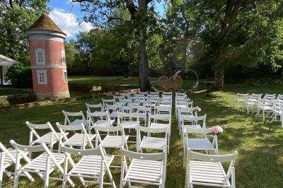Chambre lumineuse avec lit double, fauteuil gris, bureau en bois, fenêtre à carreaux et poutres apparentes.