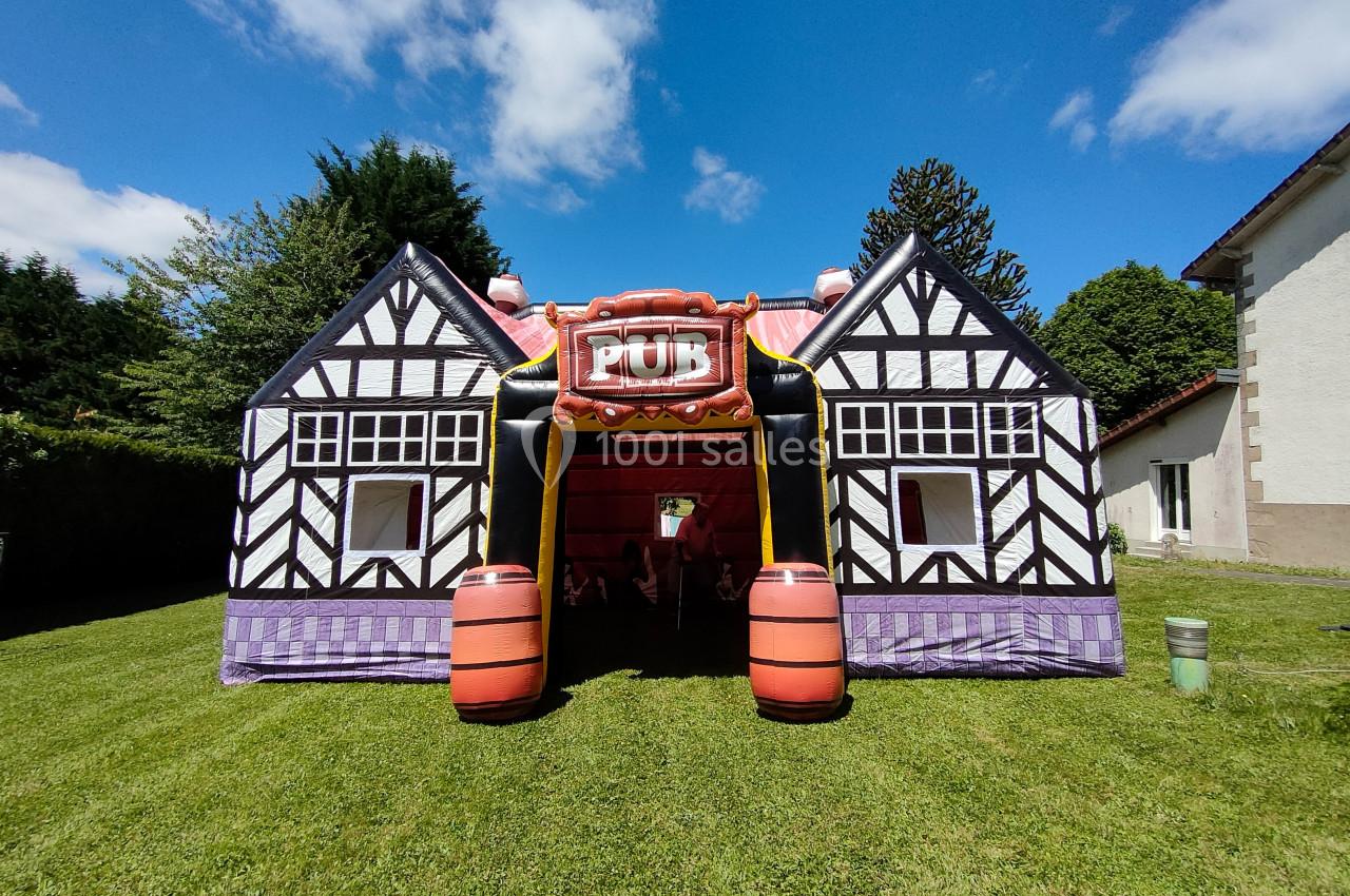Structure gonflable en forme de pub à colombages, installée sur une pelouse sous un ciel bleu.