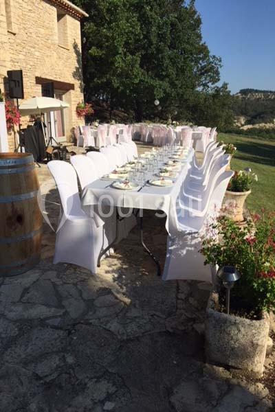 Table dressée en extérieur avec nappes blanches, chaises couvertes, et décor champêtre près d'une maison en pierre.