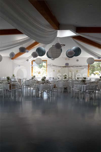 Salle décorée pour un événement avec tables dressées, chaises blanches et lanternes suspendues au plafond.