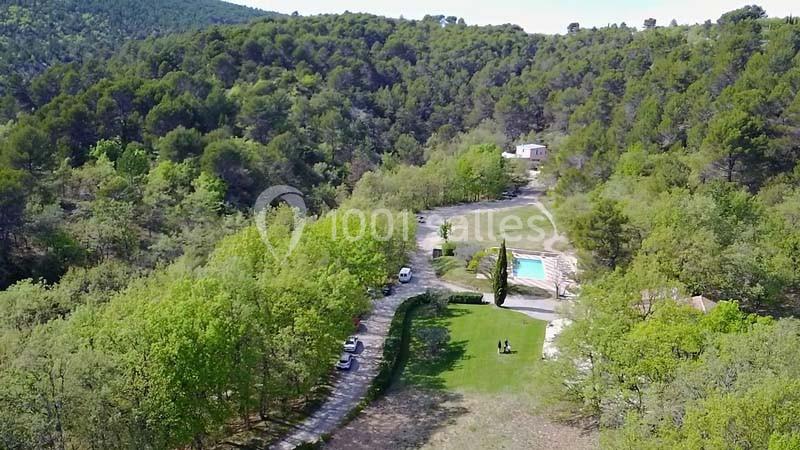 Vue aérienne d'un paysage boisé avec une piscine, une maison et une allée bordée d'arbres.