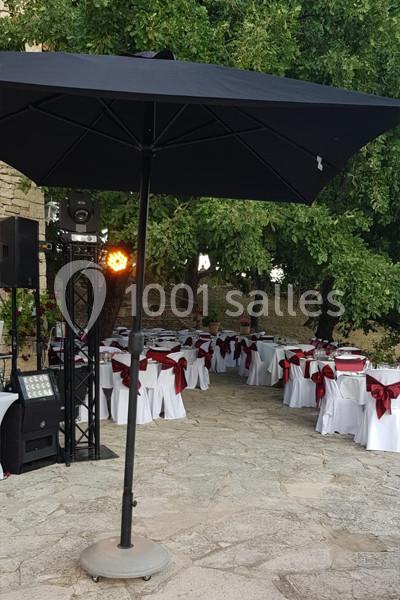 Tables dressées avec nappes blanches et nœuds rouges sous un grand parasol noir, en extérieur près d'arbres.