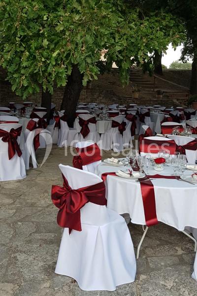 Tables et chaises blanches décorées de nœuds rouges, disposées en extérieur sous des arbres pour un événement.