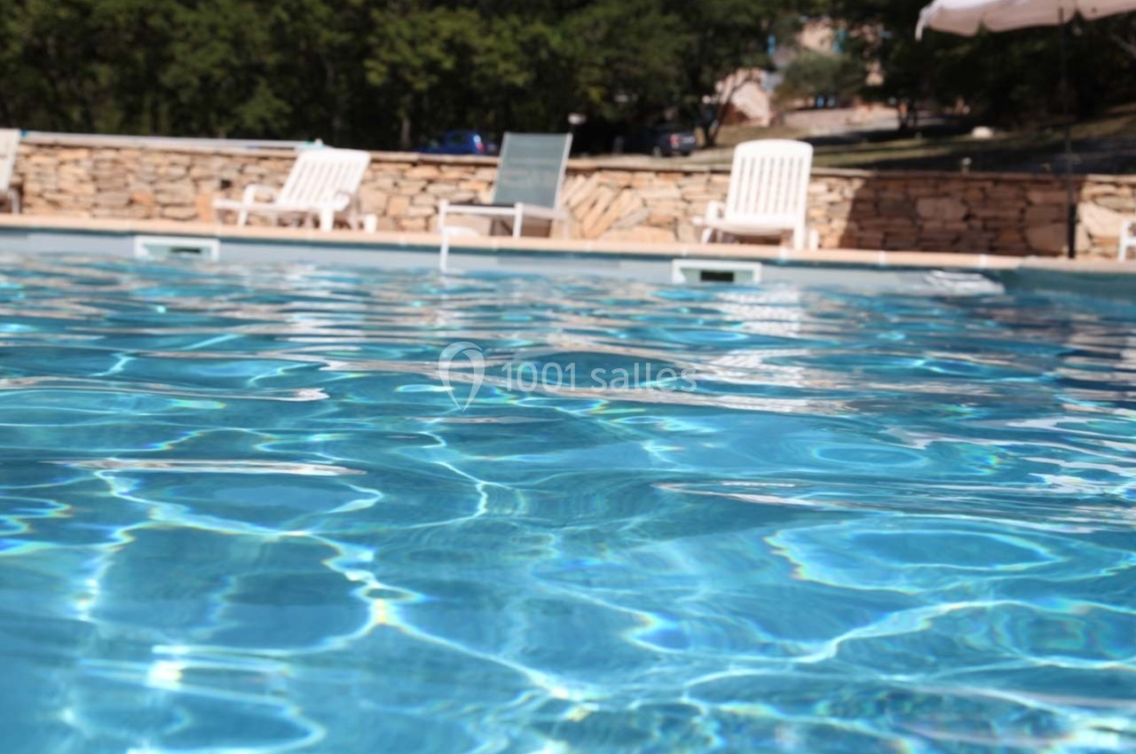 Piscine extérieure avec eau claire, entourée de chaises longues blanches et d'un mur en pierre, sous un ciel dégagé.