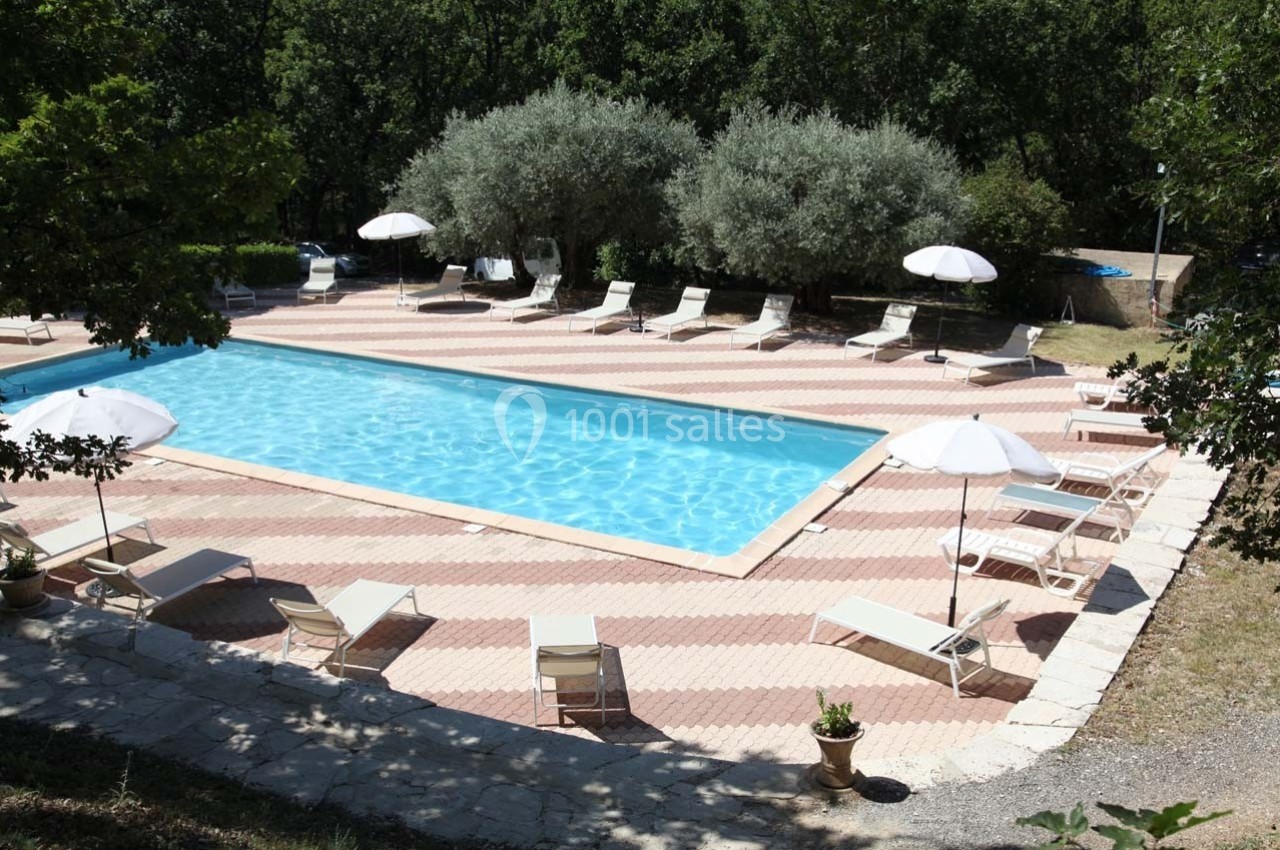 Piscine extérieure entourée de transats, parasols blancs et arbres, dans un cadre naturel.