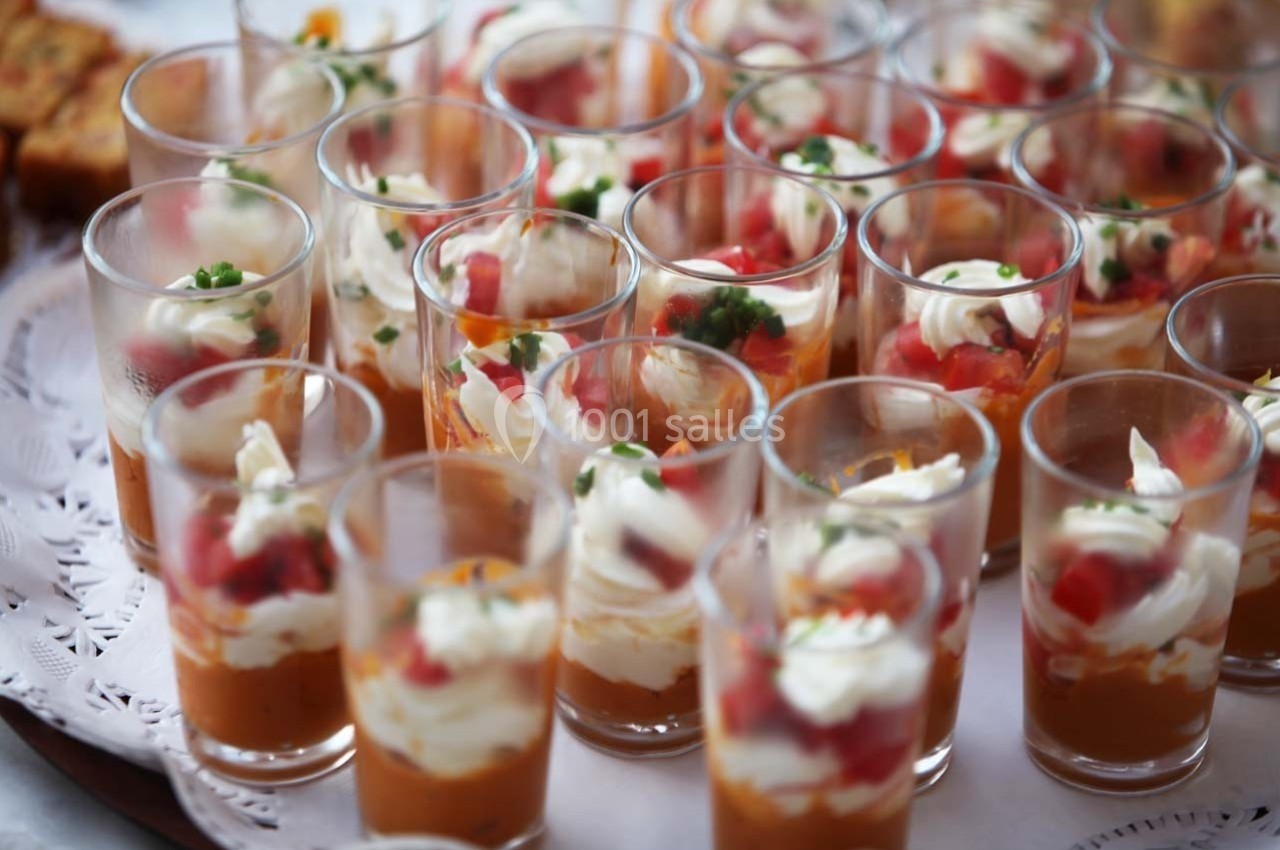 Verrines garnies de mousse orange, crème blanche, dés de tomate et herbes fraîches, disposées sur une table.