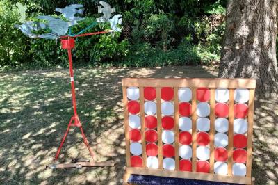 Miniature Le Rallye Loc #7 Un jeu de puissance 4 géant en bois placé sur une pelouse, à côté d'une girouette rouge sous des arbres.