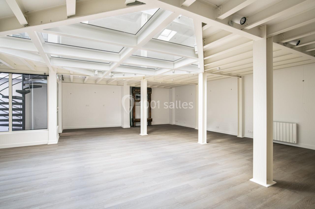 Espace intérieur lumineux avec parquet clair, poutres apparentes blanches et grandes fenêtres de toit.