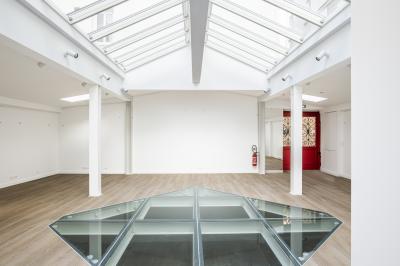 Espace intérieur lumineux avec parquet clair, verrière au plafond et ouverture en verre au sol.