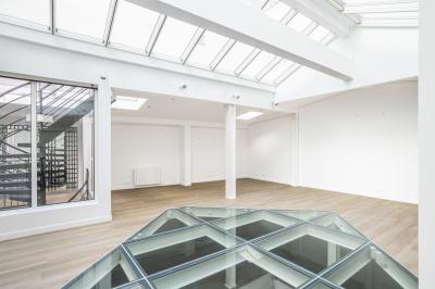 Espace intérieur lumineux avec parquet clair, verrière au plafond et ouverture en verre au sol.