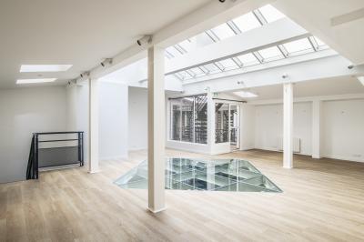 Espace intérieur lumineux avec parquet clair, verrière au plafond et ouverture en verre au sol.