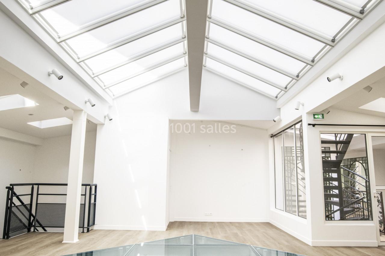 Plafond vitré laissant entrer la lumière naturelle, avec un sol en verre et un parquet clair dans un espace moderne.