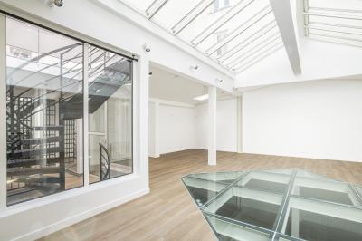 Espace intérieur lumineux avec parquet clair, verrière au plafond et ouverture vitrée au sol.