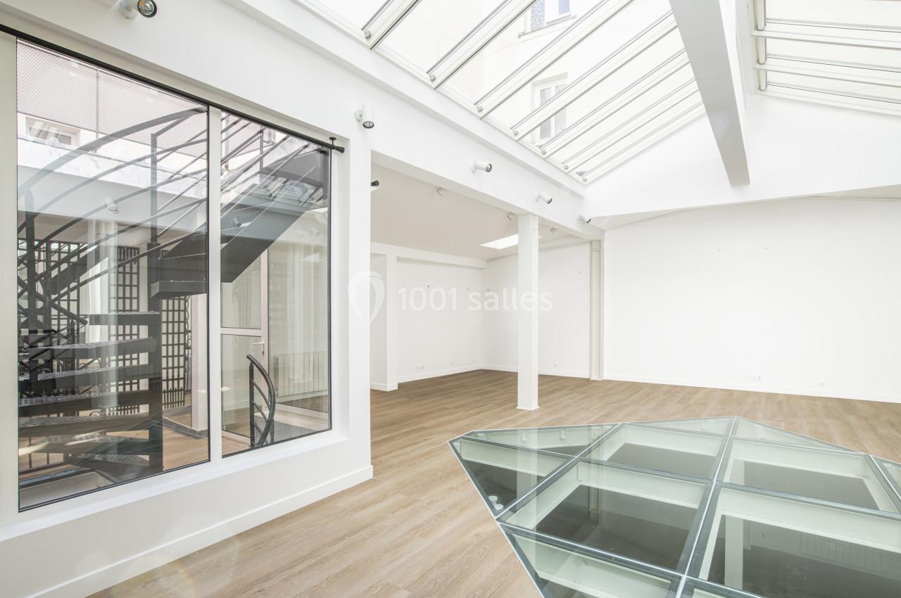 Intérieur lumineux avec parquet, verrière, escalier métallique et table en verre dans un espace moderne et épuré.