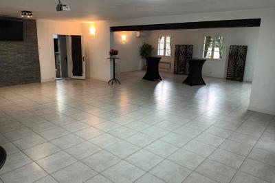 Salon lumineux avec mobilier en résine tressée, plantes vertes, tapis rond en jute et rideaux sombres.