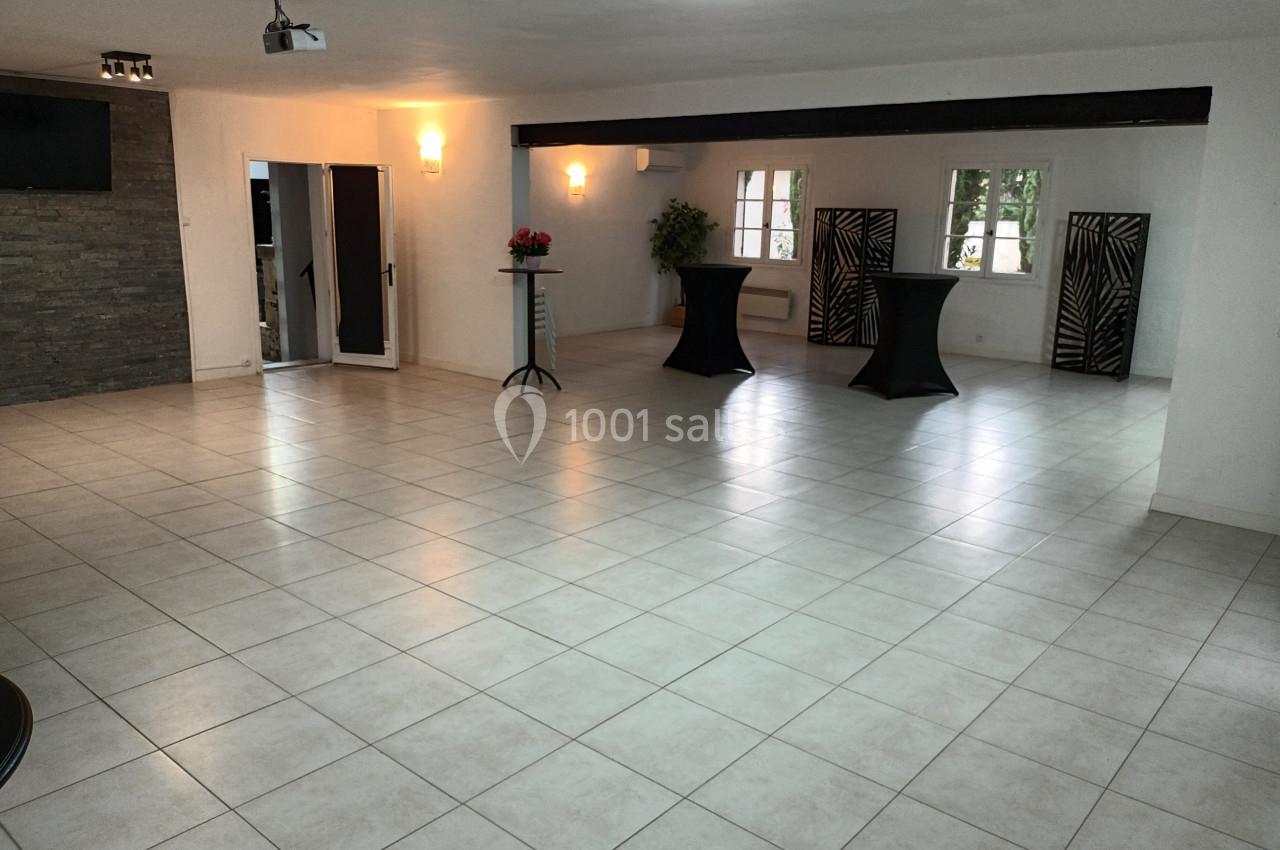 Salle lumineuse avec carrelage clair, murs blancs, tables hautes noires et fenêtres donnant sur l'extérieur.