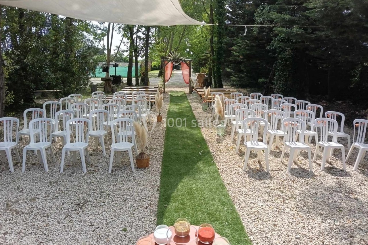 Chaises blanches disposées en rangées de part et d'autre d'une allée centrale, dans un cadre extérieur arboré.