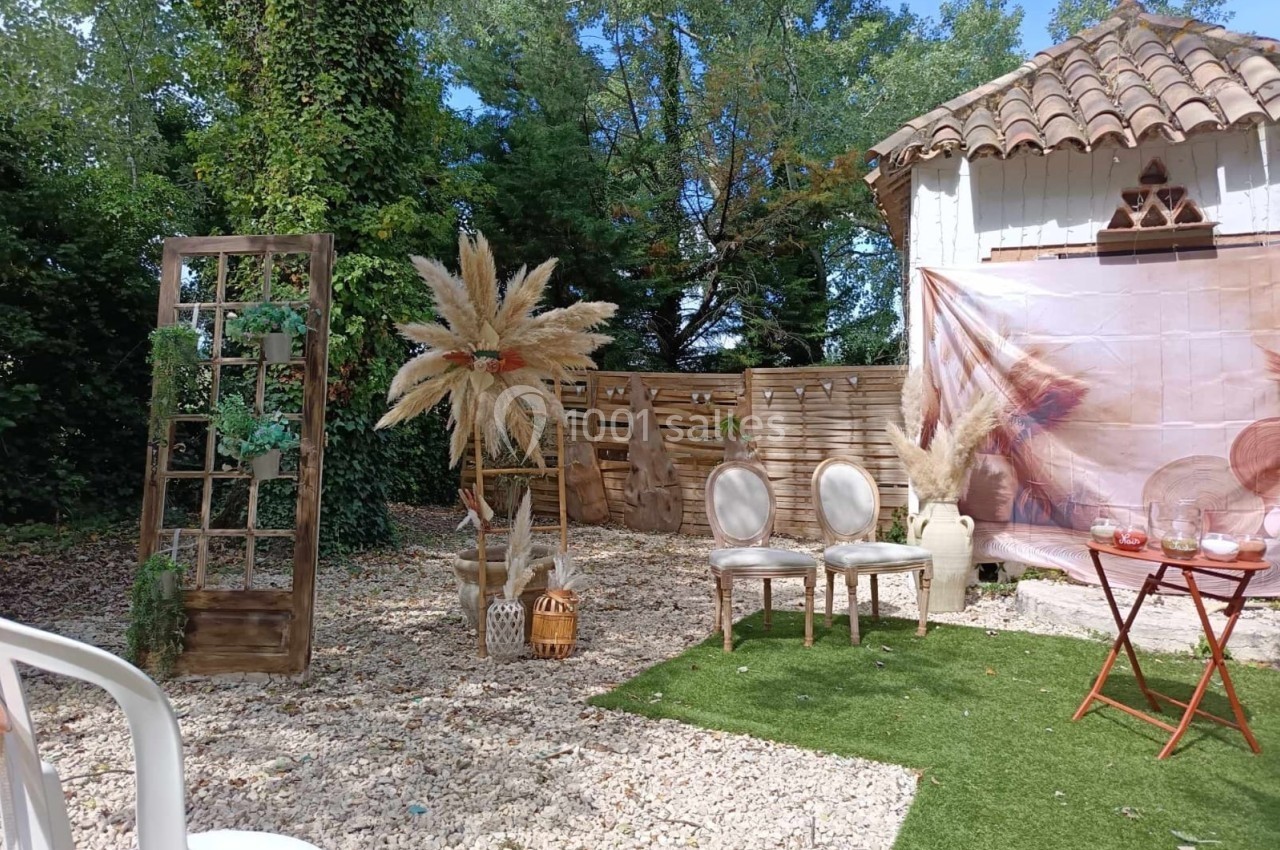 Décoration extérieure avec chaises, table, panneaux en bois et ornements végétaux dans un jardin ensoleillé.