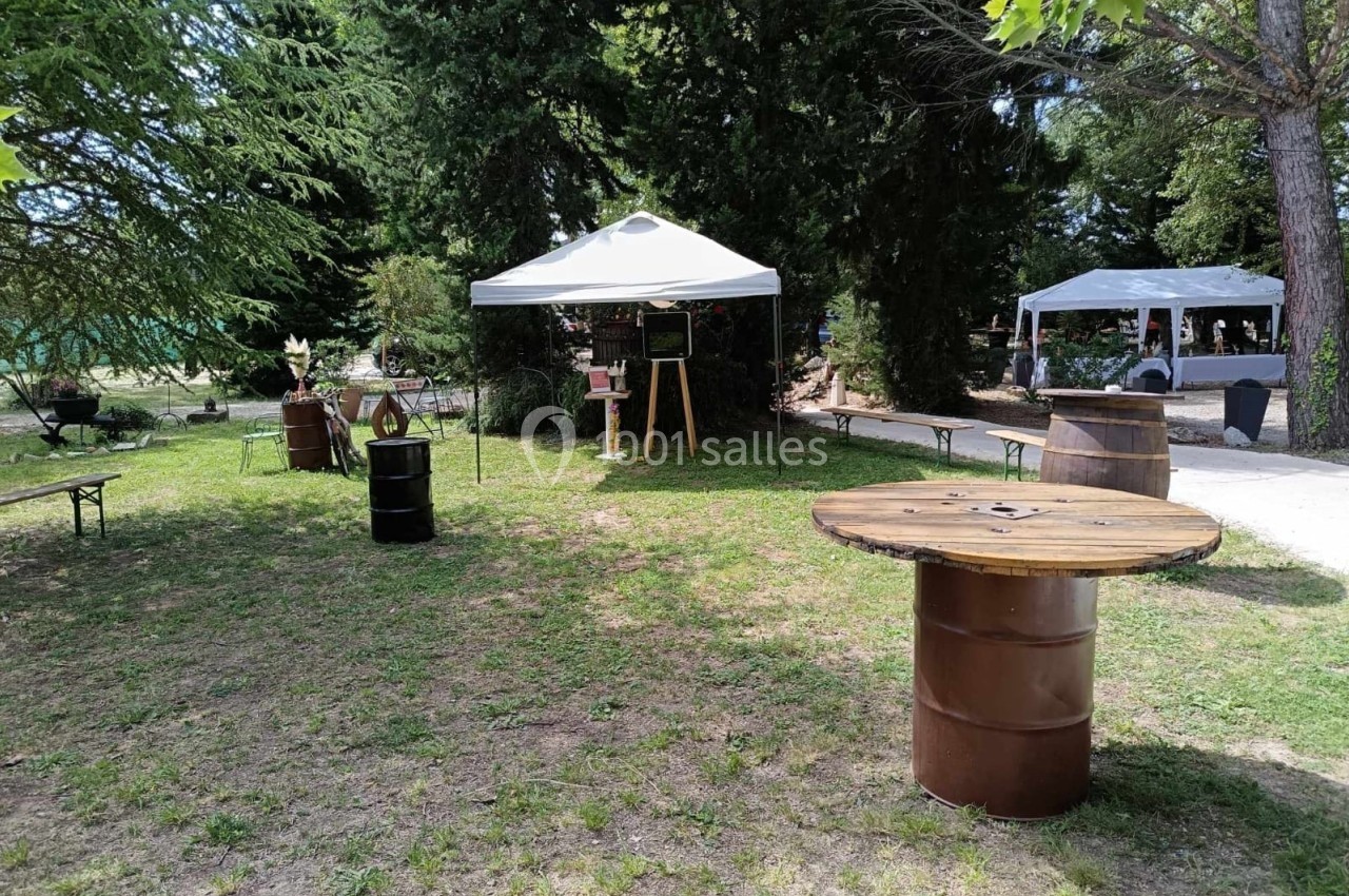 Espace extérieur avec tables en tonneaux, tentes blanches et végétation environnante dans un cadre naturel.