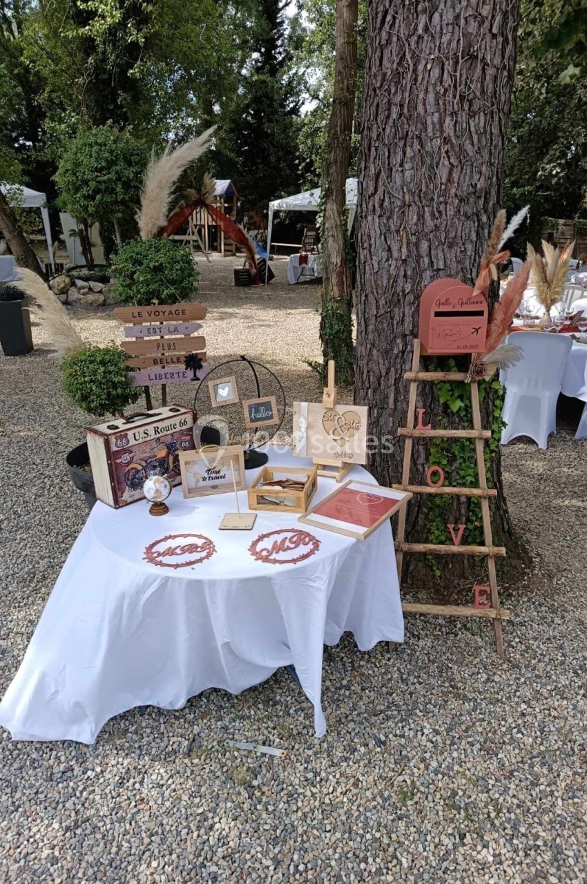 Décoration de mariage en extérieur avec table blanche, accessoires vintage, pancartes et échelle en bois ornée.