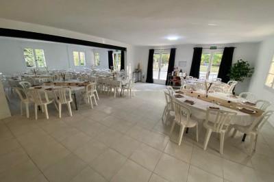 Salon lumineux avec mobilier en résine tressée, plantes vertes, tapis rond en jute et rideaux sombres.