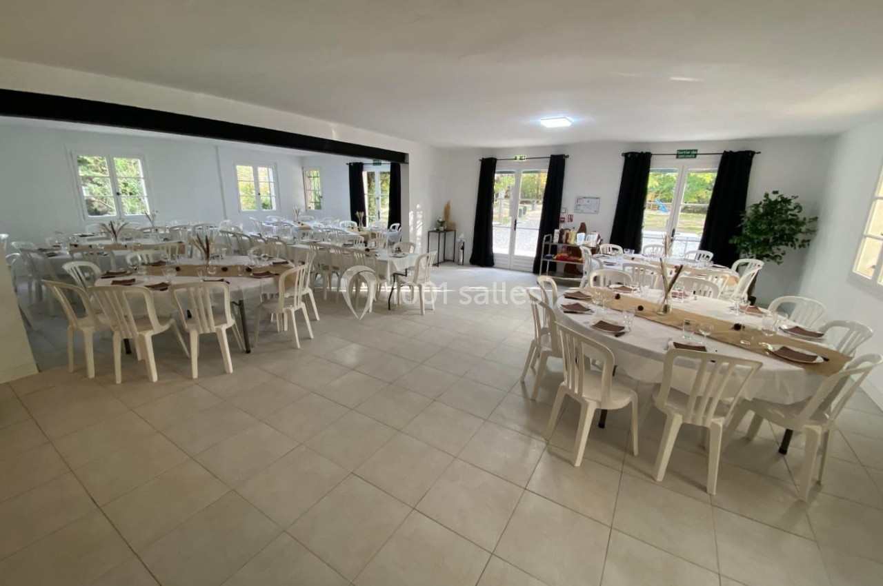 Salle lumineuse aménagée avec des tables rondes dressées et des chaises blanches, prête pour un événement.