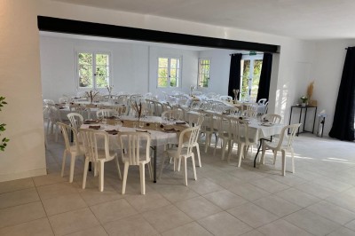 Salon lumineux avec mobilier en résine tressée, plantes vertes, tapis rond en jute et rideaux sombres.