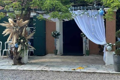 Salon lumineux avec mobilier en résine tressée, plantes vertes, tapis rond en jute et rideaux sombres.