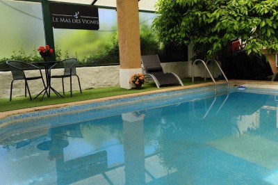 Salon lumineux avec mobilier en résine tressée, plantes vertes, tapis rond en jute et rideaux sombres.