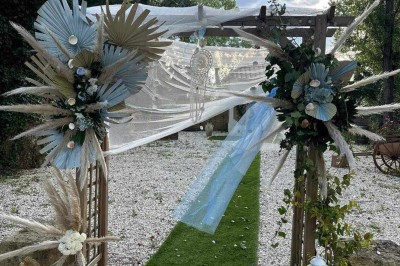 Salon lumineux avec mobilier en résine tressée, plantes vertes, tapis rond en jute et rideaux sombres.