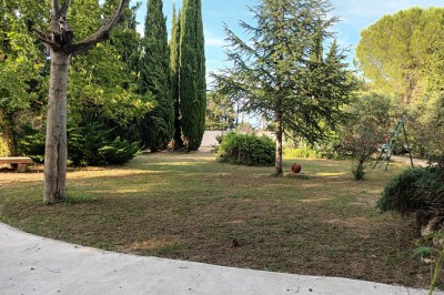 Salon lumineux avec mobilier en résine tressée, plantes vertes, tapis rond en jute et rideaux sombres.