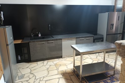 Salon lumineux avec mobilier en résine tressée, plantes vertes, tapis rond en jute et rideaux sombres.