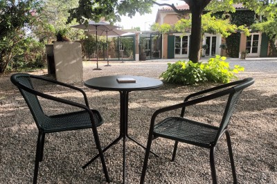 Salon lumineux avec mobilier en résine tressée, plantes vertes, tapis rond en jute et rideaux sombres.