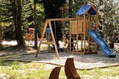 Salon lumineux avec mobilier en résine tressée, plantes vertes, tapis rond en jute et rideaux sombres.