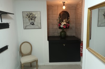 Salon lumineux avec mobilier en résine tressée, plantes vertes, tapis rond en jute et rideaux sombres.