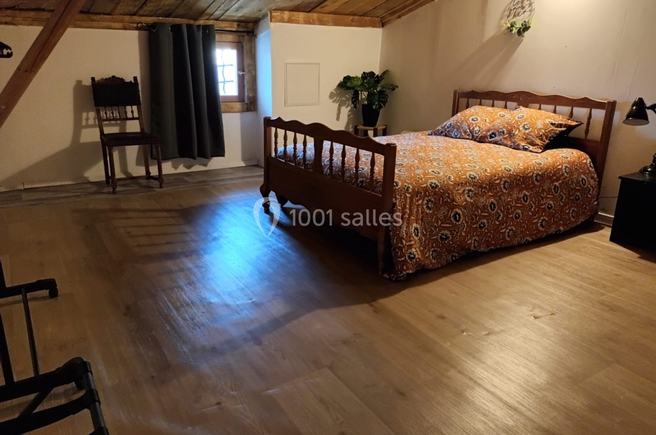 Chambre mansardée avec lit double, couvre-lit à motifs, parquet en bois, chaise ancienne et petite fenêtre.