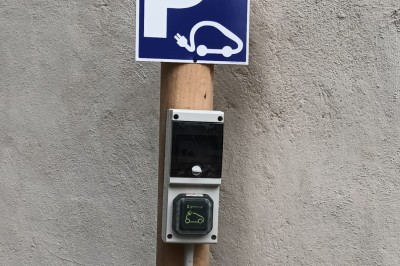 Salon lumineux avec mobilier en résine tressée, plantes vertes, tapis rond en jute et rideaux sombres.