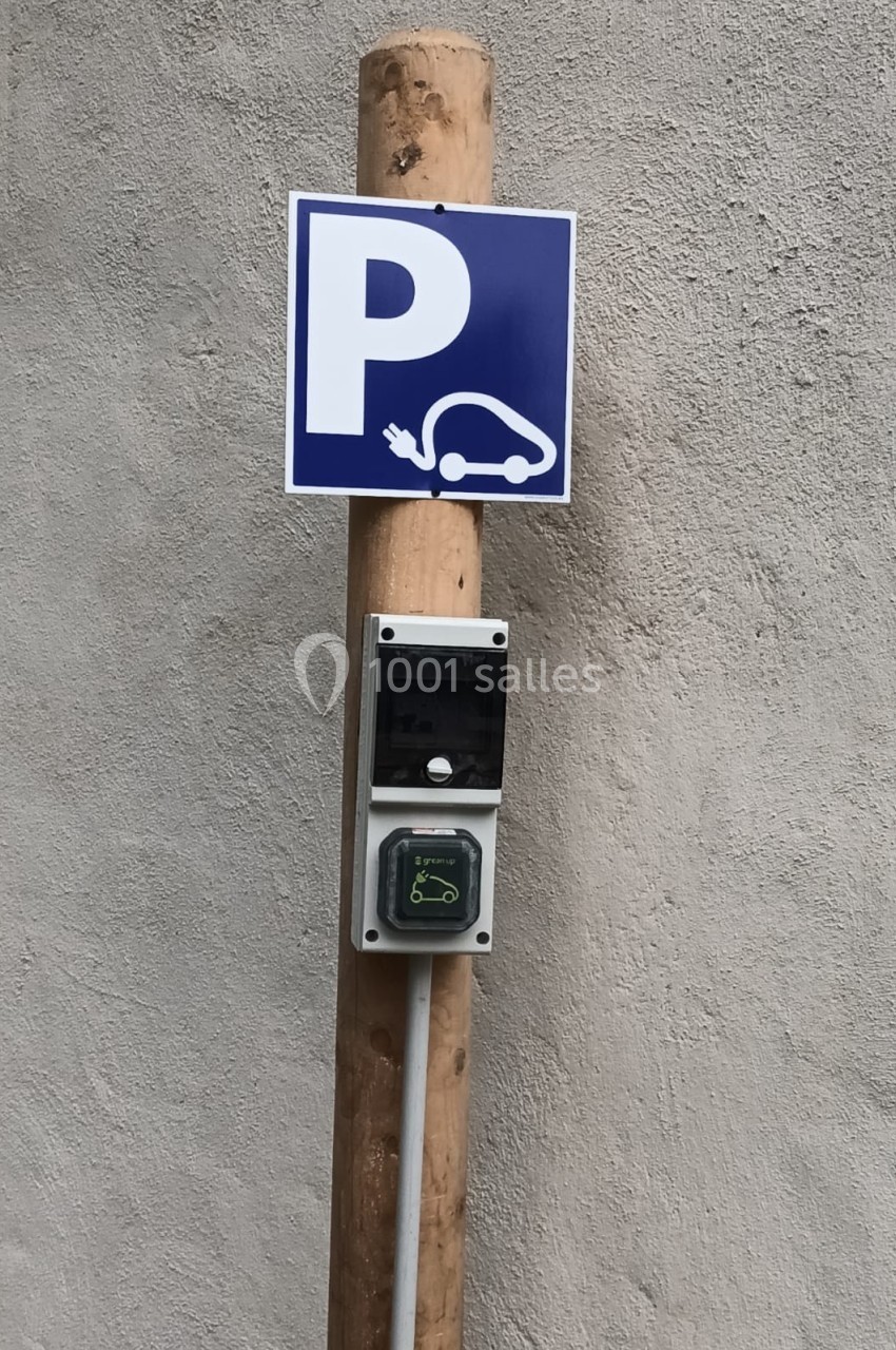 Borne de recharge électrique fixée sur un poteau en bois avec un panneau indiquant un parking pour véhicules électriques.