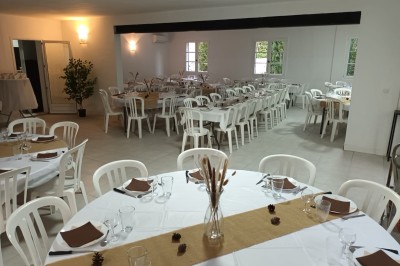 Salon lumineux avec mobilier en résine tressée, plantes vertes, tapis rond en jute et rideaux sombres.