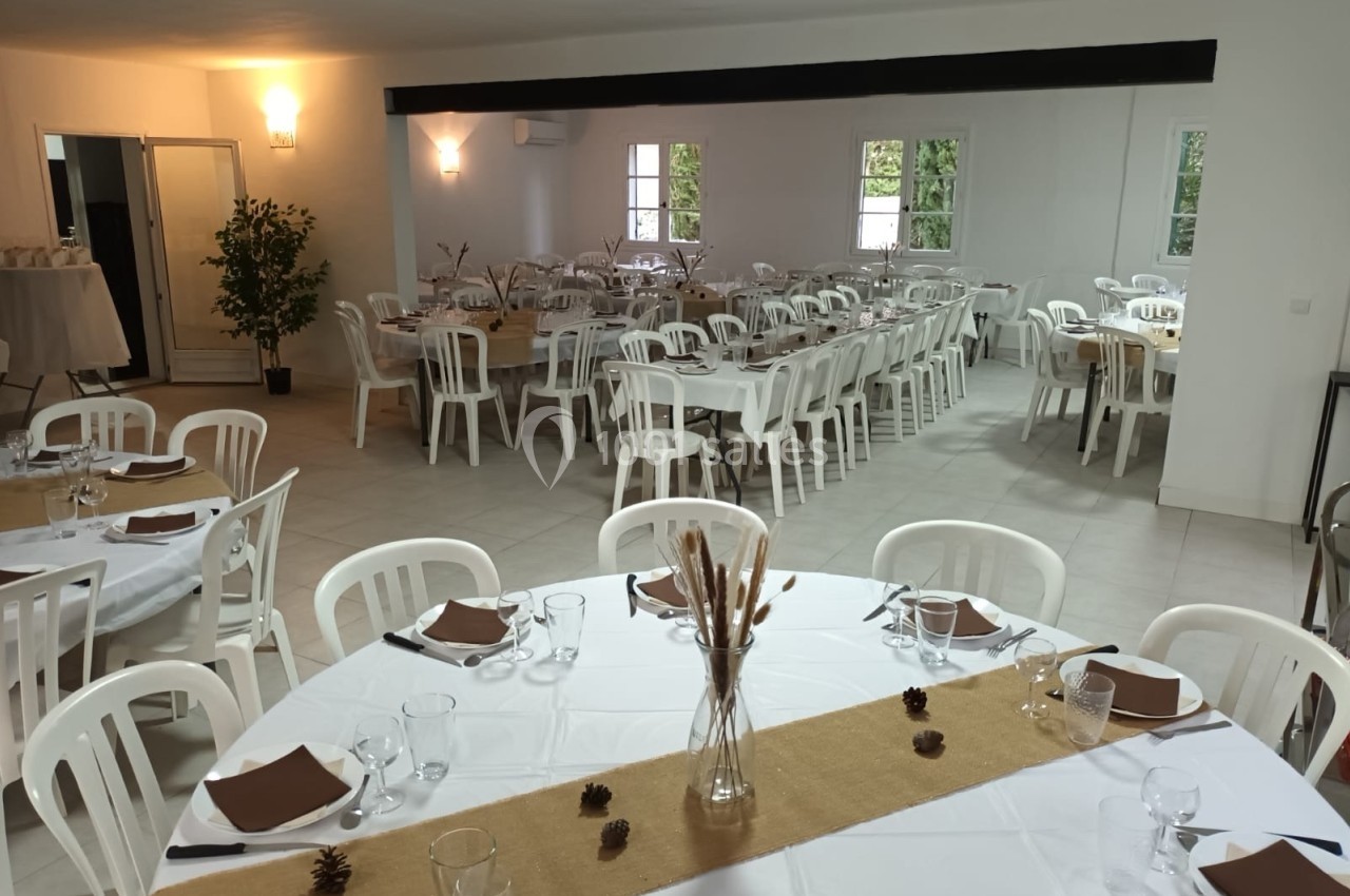 Salle de réception lumineuse avec tables rondes et rectangulaires dressées, décorations simples et chaises blanches.