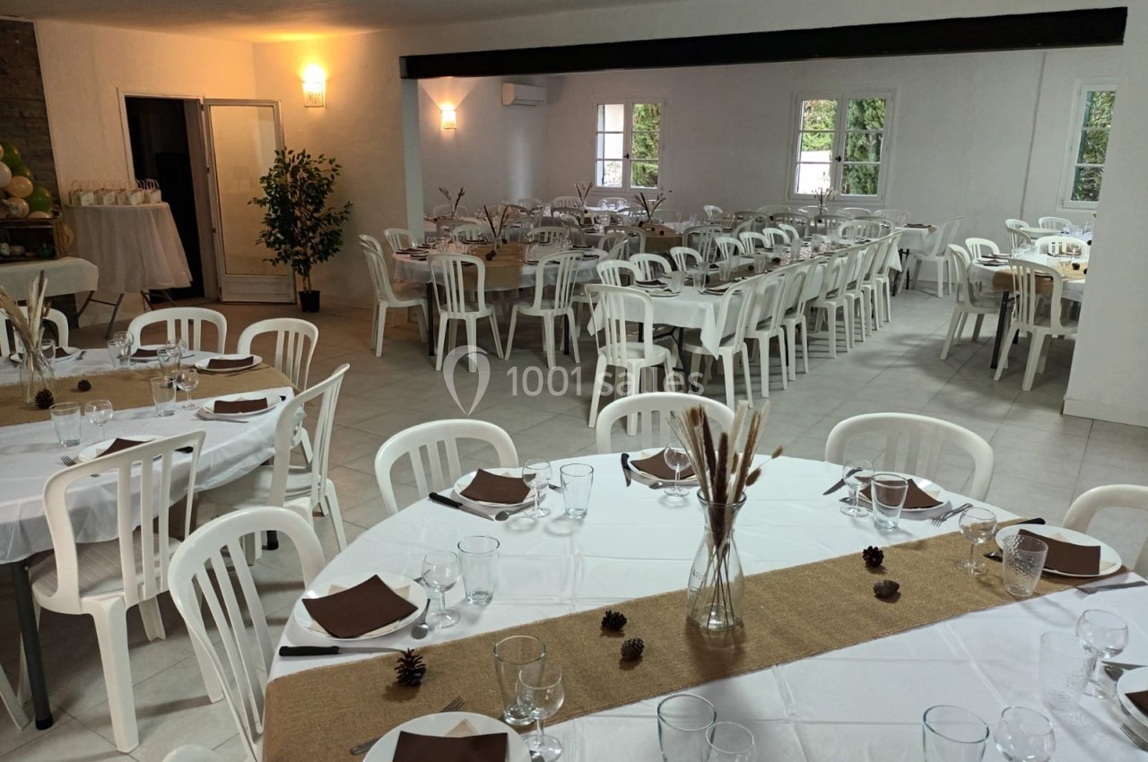 Salle de réception décorée avec des tables dressées, nappes blanches, chemins de table en jute et chaises blanches.
