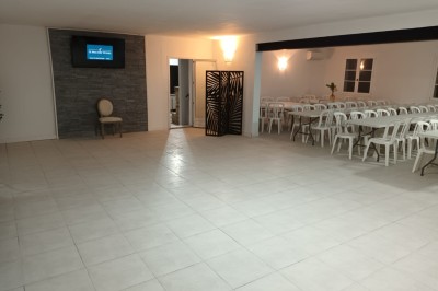 Salon lumineux avec mobilier en résine tressée, plantes vertes, tapis rond en jute et rideaux sombres.