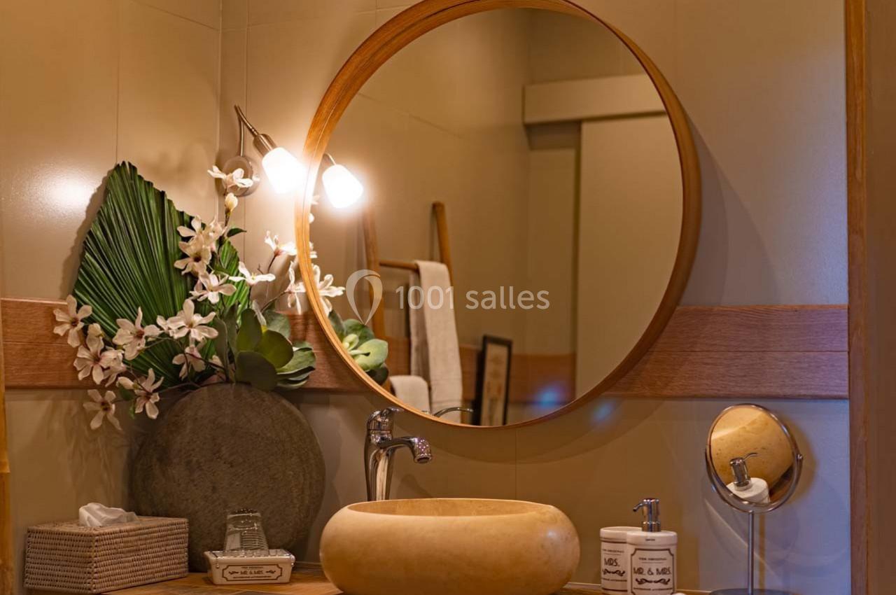 Salle de bain avec miroir rond, vasque en pierre, plantes décoratives et éclairage doux.