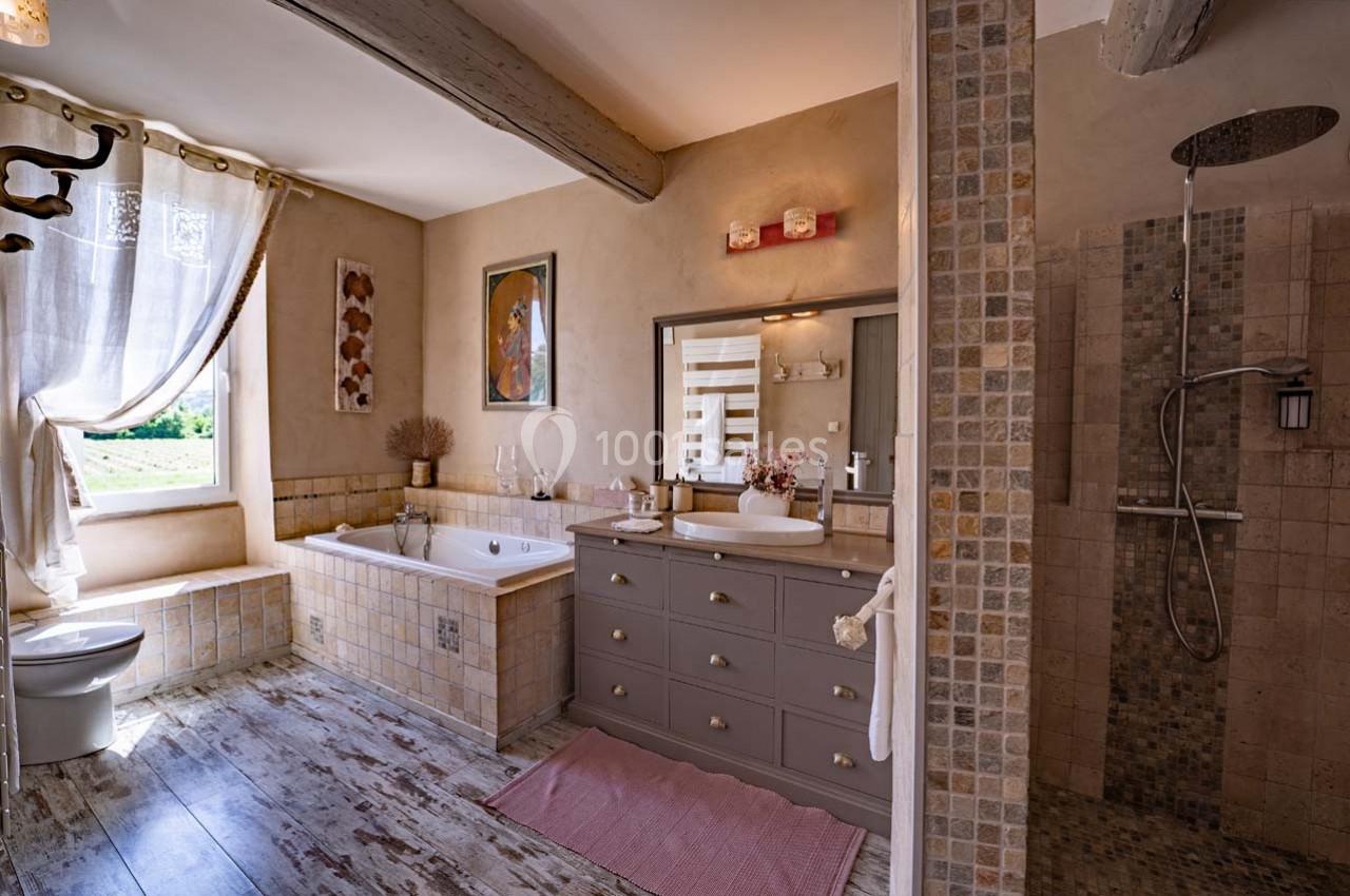Salle de bain lumineuse avec baignoire, douche à l'italienne, meuble vasque gris et sol en bois clair.