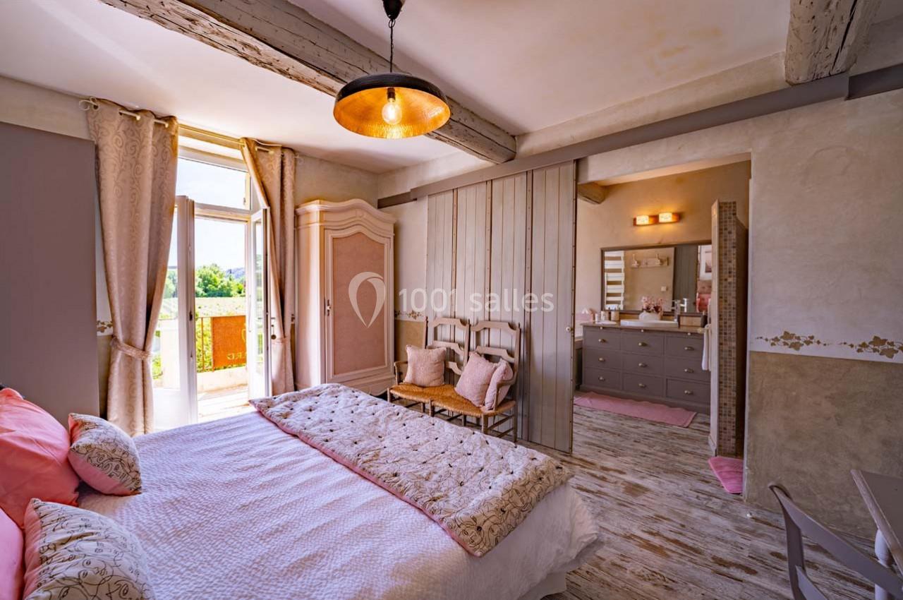 Chambre lumineuse avec lit double, armoire en bois, commode, et vue sur un balcon donnant sur un paysage verdoyant.