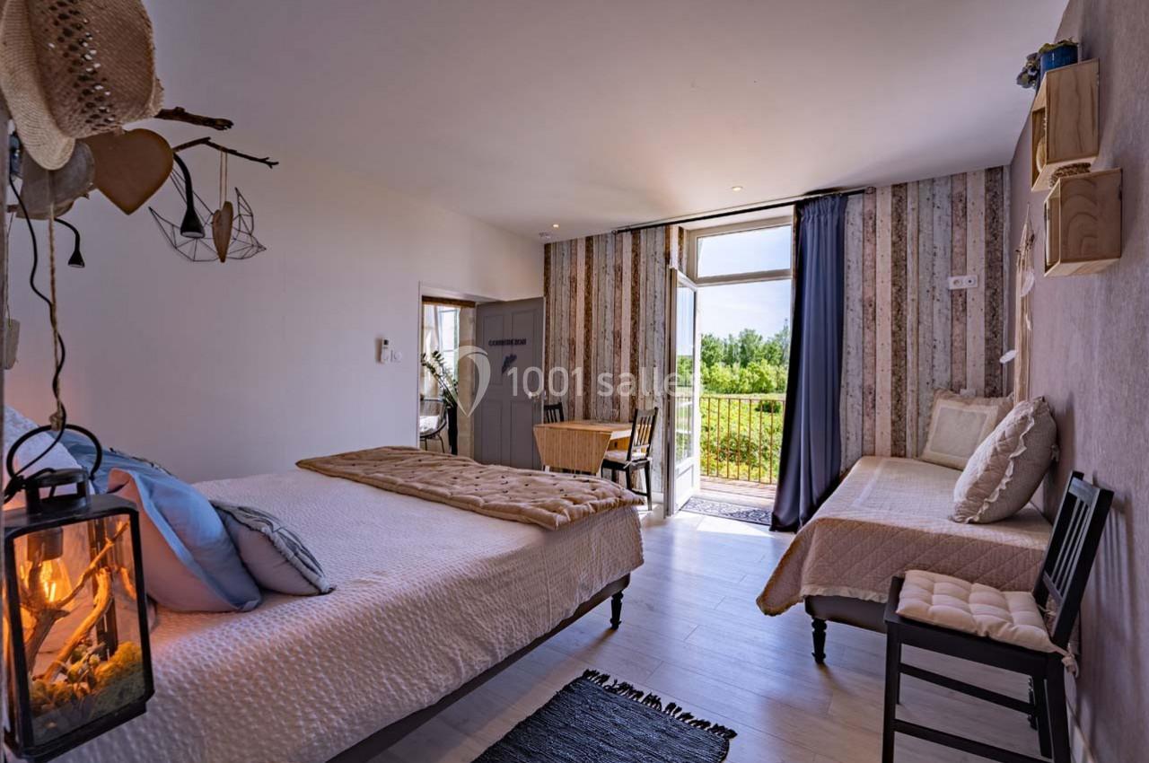 Chambre lumineuse avec lit double, lit simple, décoration chaleureuse et vue sur un balcon donnant sur un espace vert.