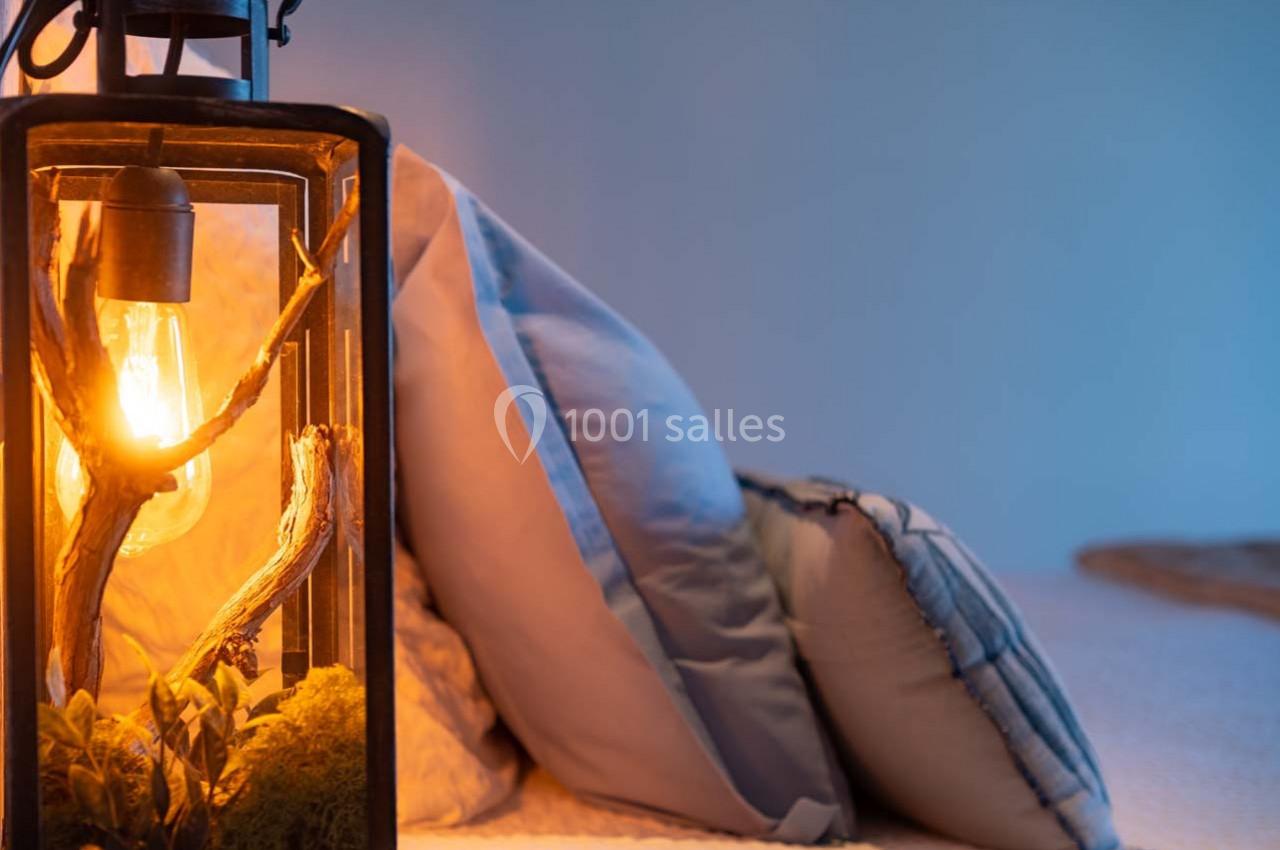 Lampe décorative avec ampoule chaude et branches en bois, posée près de coussins bleus sur un lit.